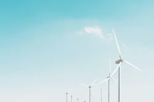a row of wind turbines against a pale blue sky