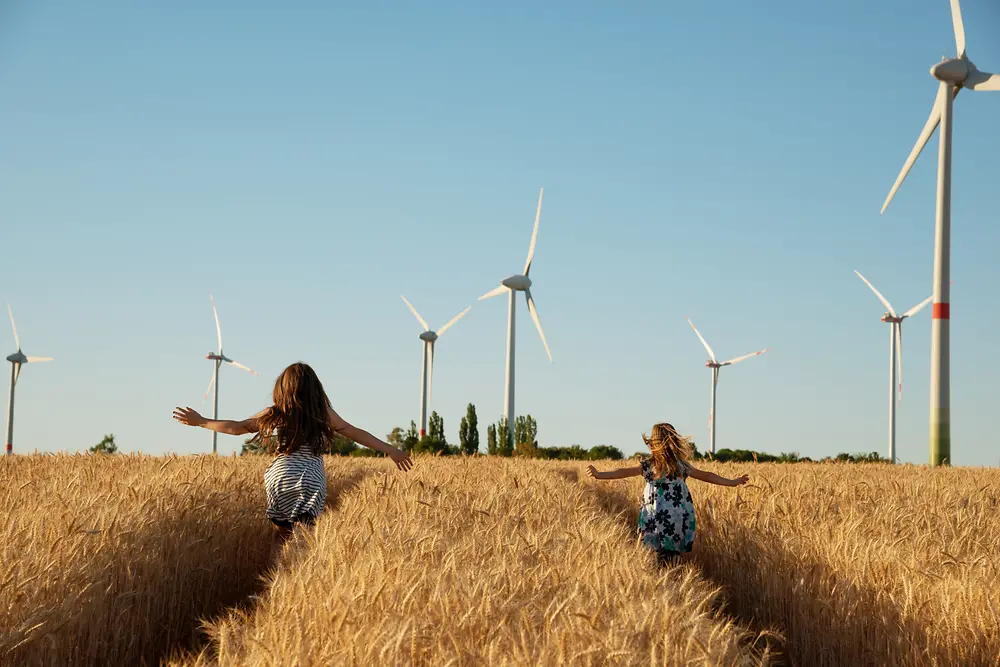 Dziewczynki biegną przez pole w kierunku turbin wiatrowych.