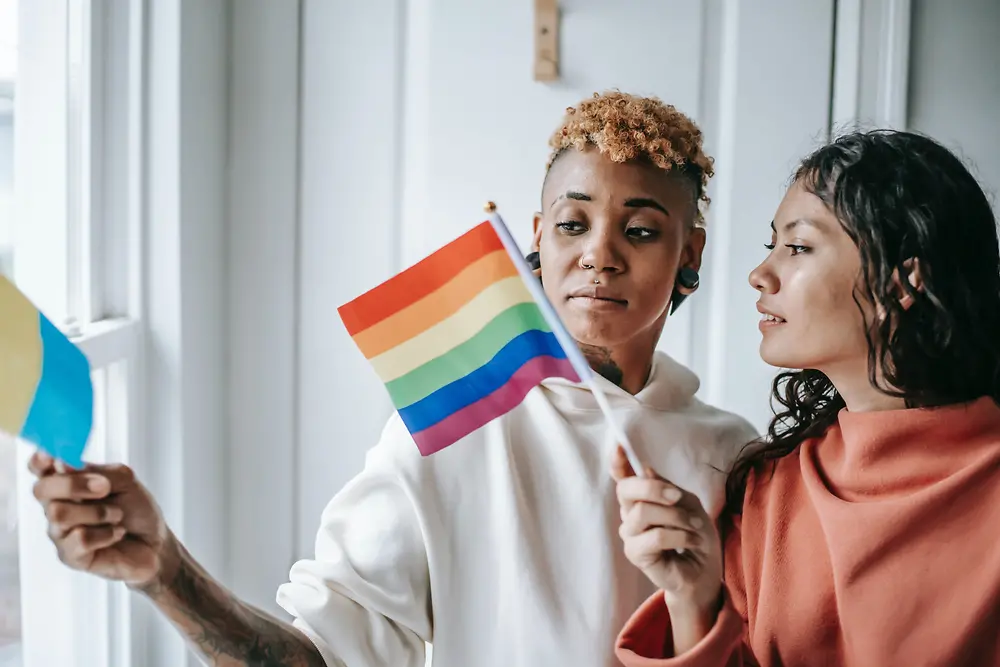 Dwie kobiety rozmawiają ze sobą i trzymające flagę LGBTQ+.
