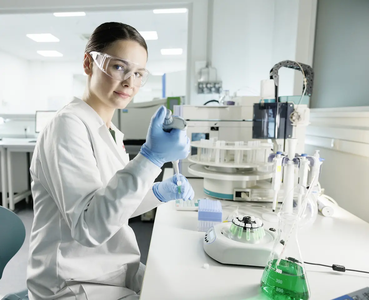 A female scientist is experimenting in a lab, wearing a lab coat and safety goggles.