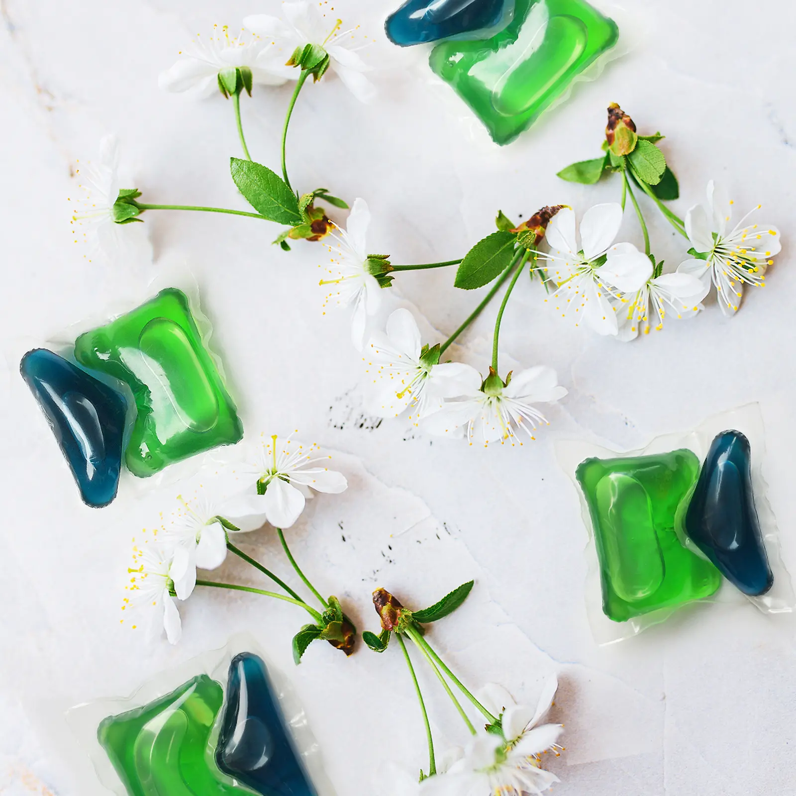 Dwie zielono-niebieskie kapsułki Henkel Persil z kwiatami wiśni dookoła