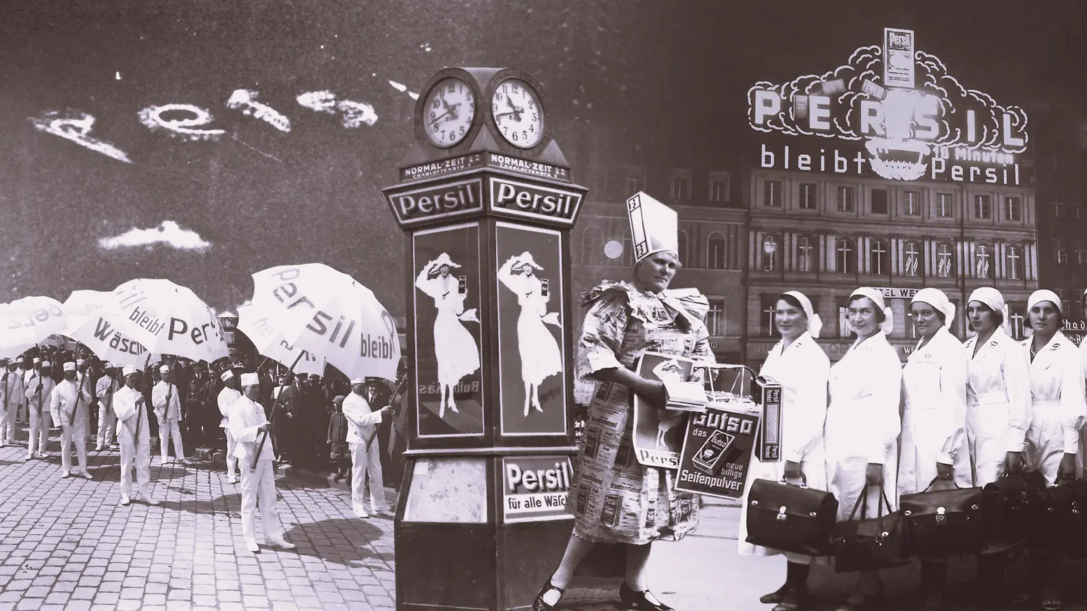 Kolaż reklamowy Persil w stylu retro, przedstawiający ludzi z parasolami z logo marki, zegar z plakatami oraz budynek z podświetlanym szyldem Persil w tle.