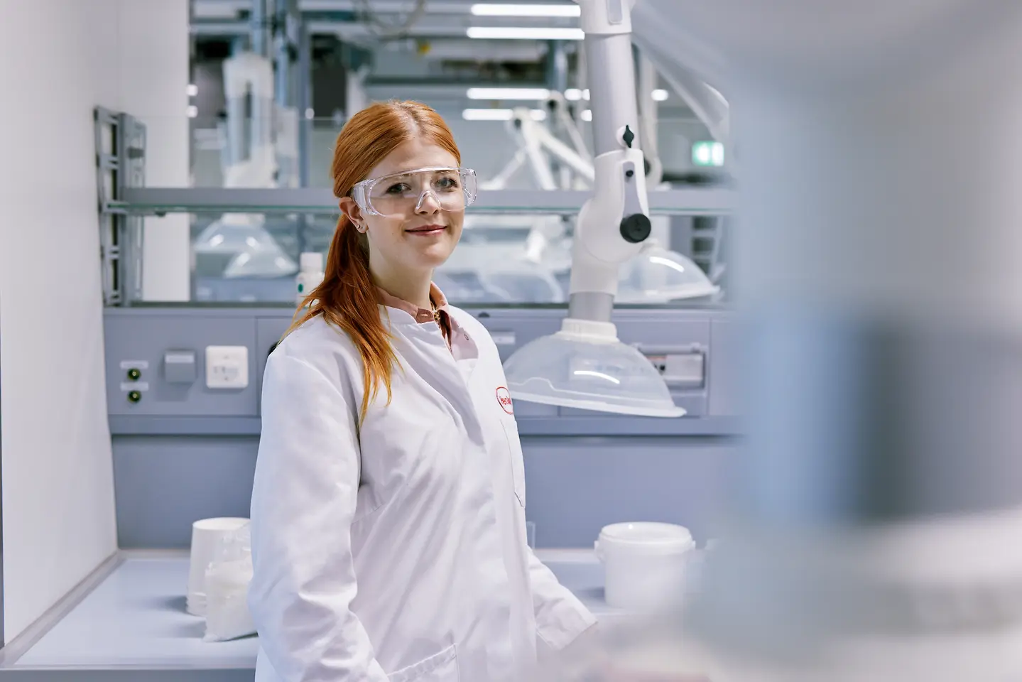 Absolwent rozpoczynający karierę w Henklu, ubrany w biały fartuch laboratoryjny, stojący w nowoczesnym laboratorium z wyposażeniem technicznym w tle.