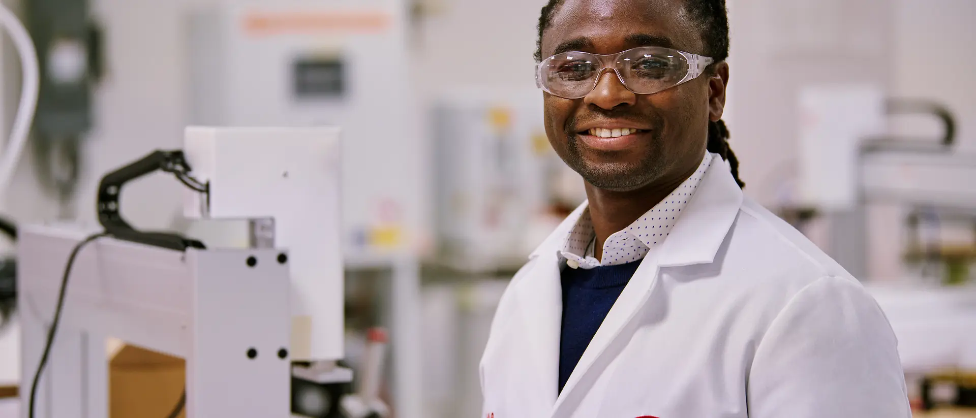 Osoba w białym fartuchu laboratoryjnym firmy Henkel stojąca w laboratorium, otoczona sprzętem i maszynami.